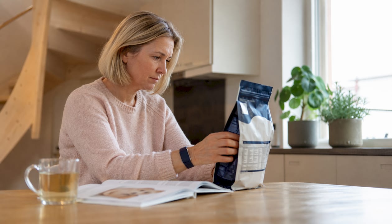 En kvinne står inne og leser nøye på innholdsfortegnelsen til hundematen.