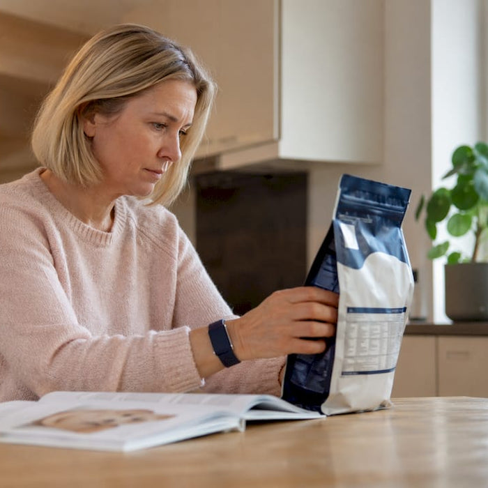En kvinne står inne og leser nøye på innholdsfortegnelsen til hundematen.